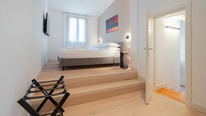 Um quarto com cama, escada, porta e luminária fixada na parede.