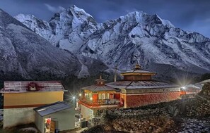 A traditional building with a red and yellow facade, situated in a mountainous area with snow-covered peaks in the background. - Trekkers Holiday Inn (Panboche)