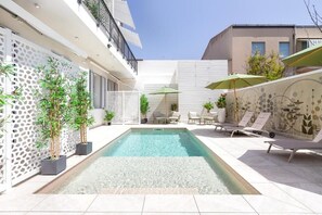 Una piscina al aire libre, sombrillas, sillones reclinables de piscina