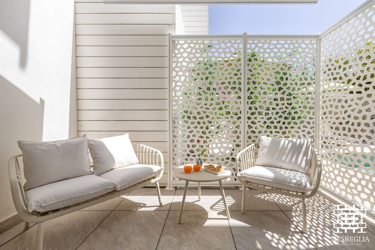 A modern outdoor seating area with white furniture, a decorative white partition, and a small table with a vase and orange drink.