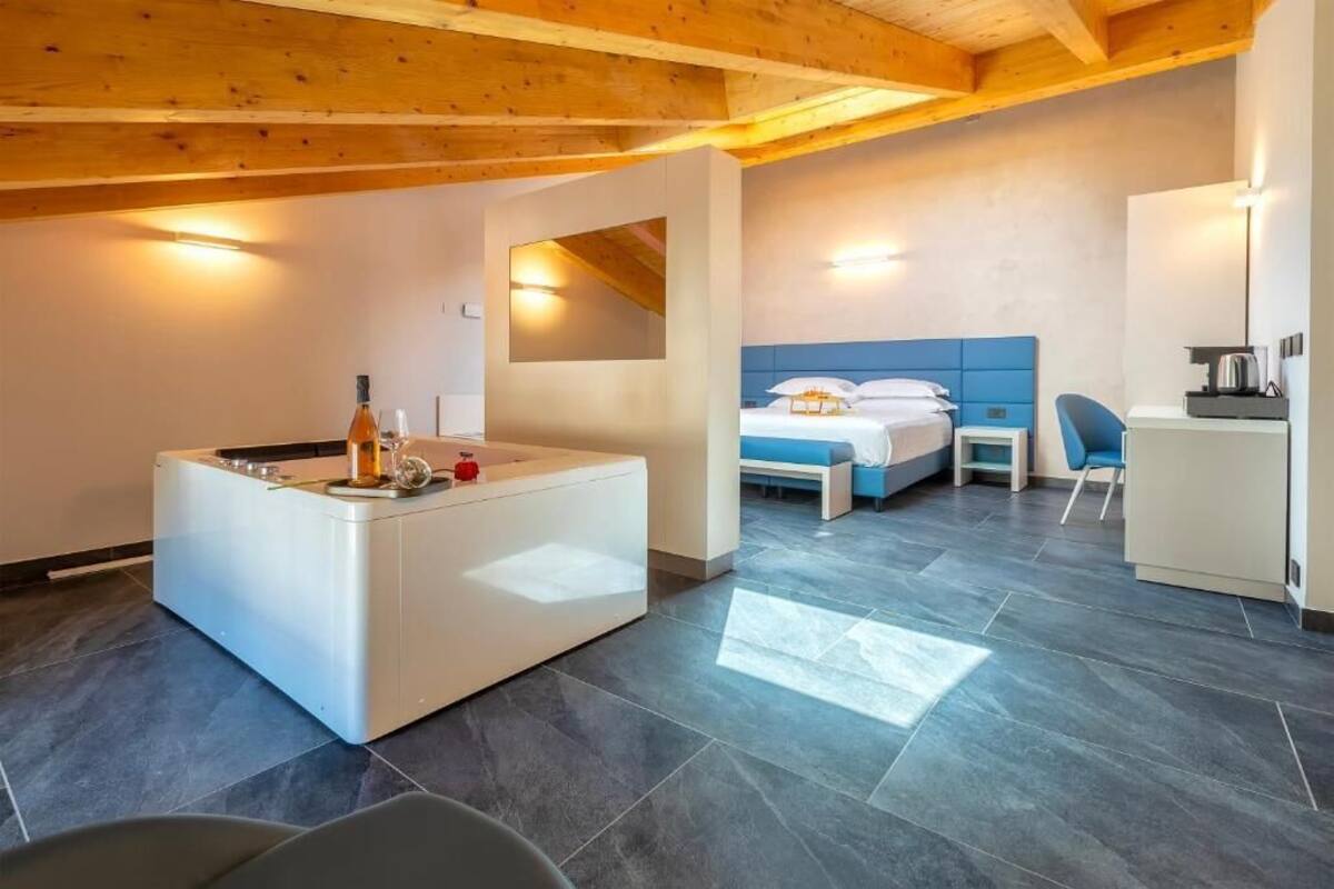A modern hotel room with a large bathtub, a bed with blue headboard, a desk, and a chair.