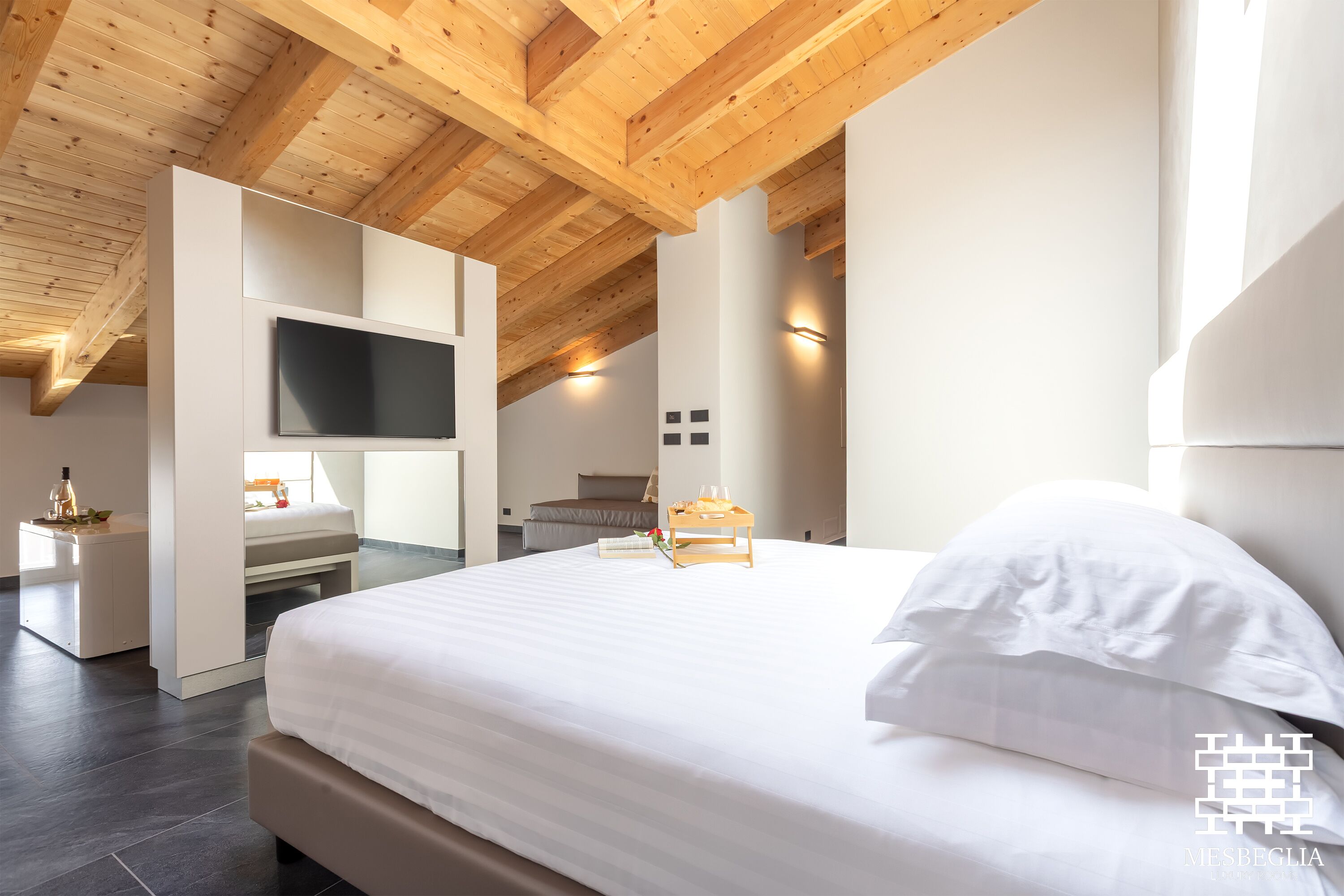 Een moderne slaapkamer met een groot bed, een aan de muur bevestigde televisie en een houten plafond.