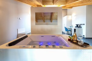 Un bagno moderno con una grande vasca, un soffitto in legno e, sullo sfondo, un piccolo angolo cottura.