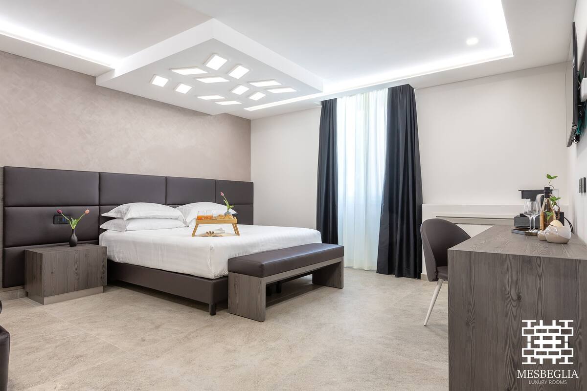 A modern bedroom with a bed, bedside tables, a desk, and a ceiling light fixture.