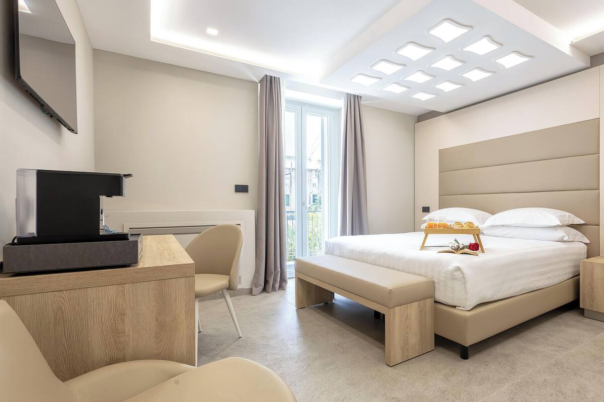 A modern hotel room with a bed, bedside tables, a desk, and a chair.
