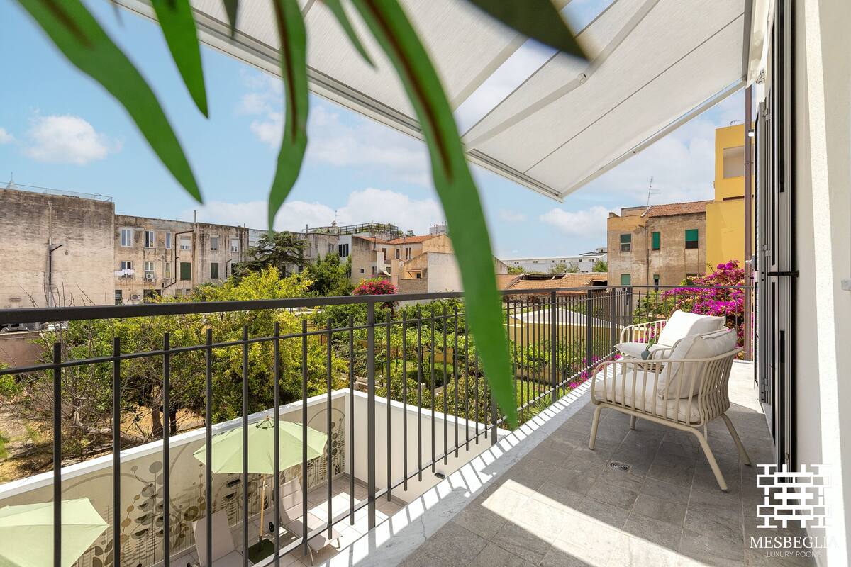 A balcony with a view of surrounding buildings, a table with chairs, and a white chair with cushions.