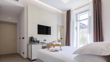 A hotel room with a bed, a desk with a flat-screen TV, a coffee machine, and a window with curtains.