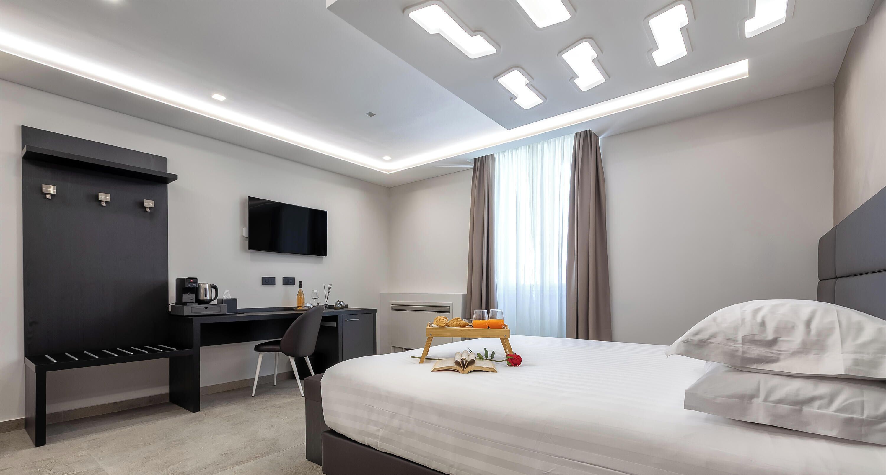 A modern hotel room with a large bed, a desk, a flat-screen TV, and a coffee machine.