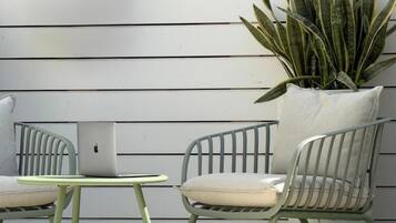 Een terras met twee stoelen, een kleine tafel, een potplant en een laptop tegen een witte muur.