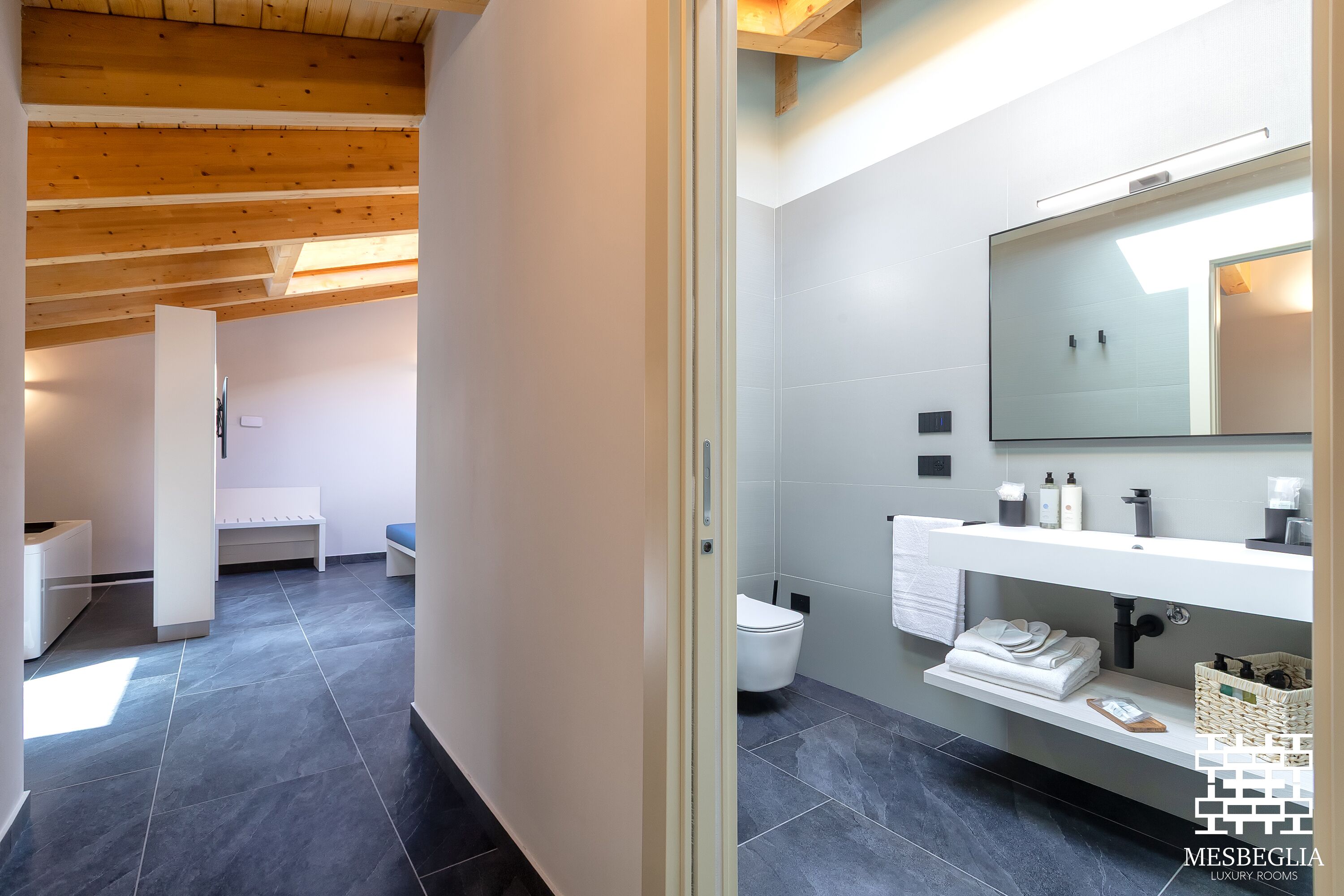 Un baño moderno con un espejo grande, sanitarios blancos y piso de baldosas.