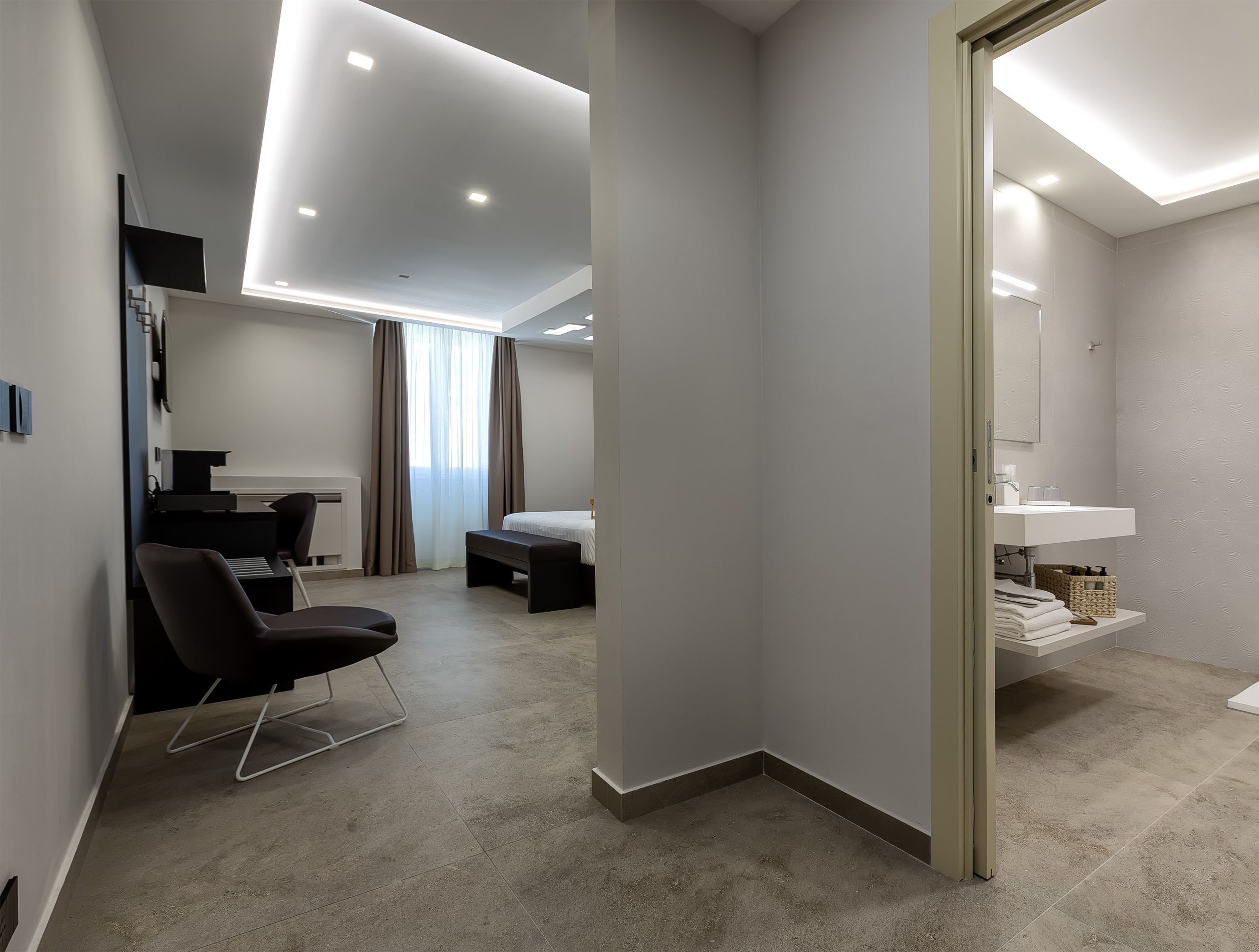A modern hotel room with a minimalist design, featuring a large bed, a desk, and a seating area.