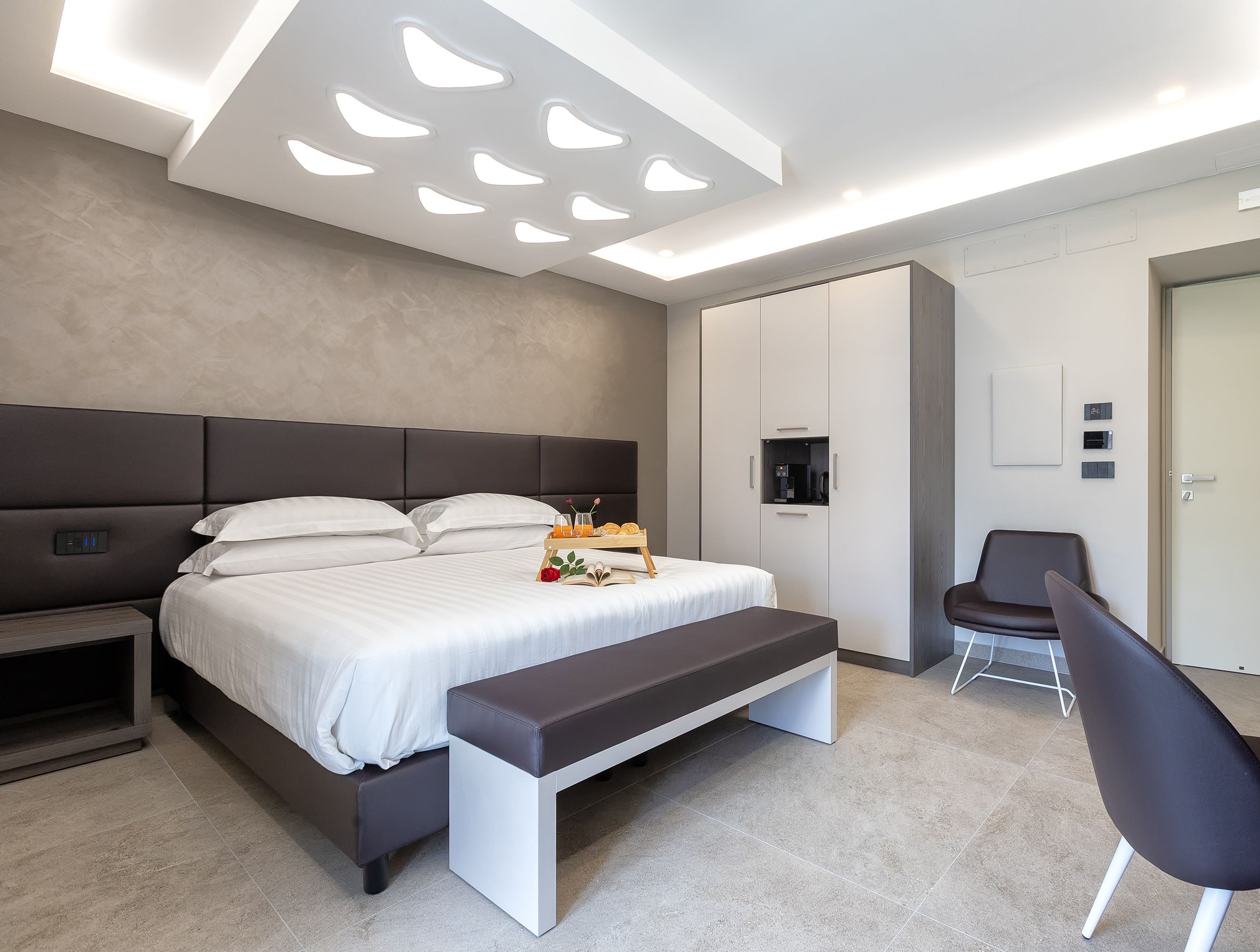 Ein modernes Schlafzimmer mit einem großen Bett, Nachttischen, einer Bank, einem Sessel und einem Kleiderschrank.