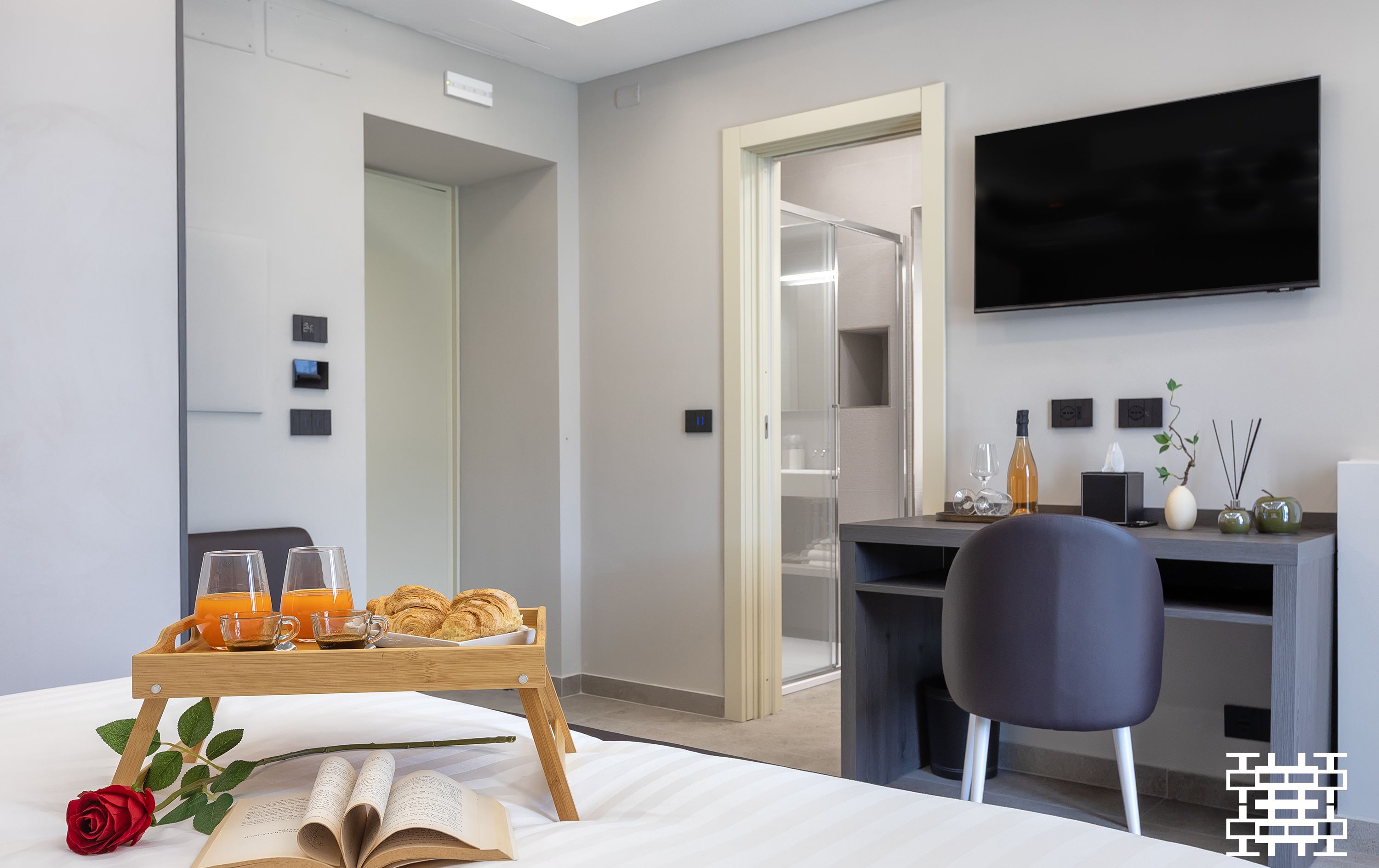 A modern hotel room with a bed, a tray with breakfast items, a rose, and an open book.