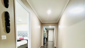 A hallway with a wooden floor, a bed with a grey headboard, and a white door.