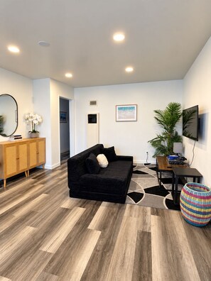 Sala de estar moderna com um sofá preto, armário de madeira e uma grande planta em vaso.