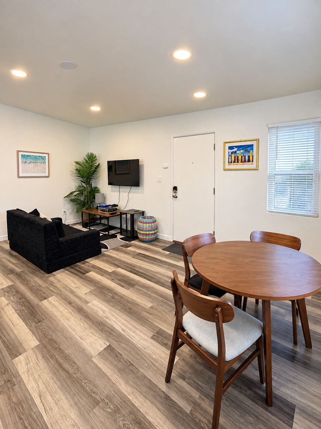 A modern living room with a black sofa, wooden dining table, and a flat-screen TV mounted on the wall.