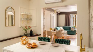 Une cuisine moderne avec un plan de travail en marbre, un coin repas avec des chaises recouvertes d’un tissu vert, et un salon avec un canapé de couleur turquoise.