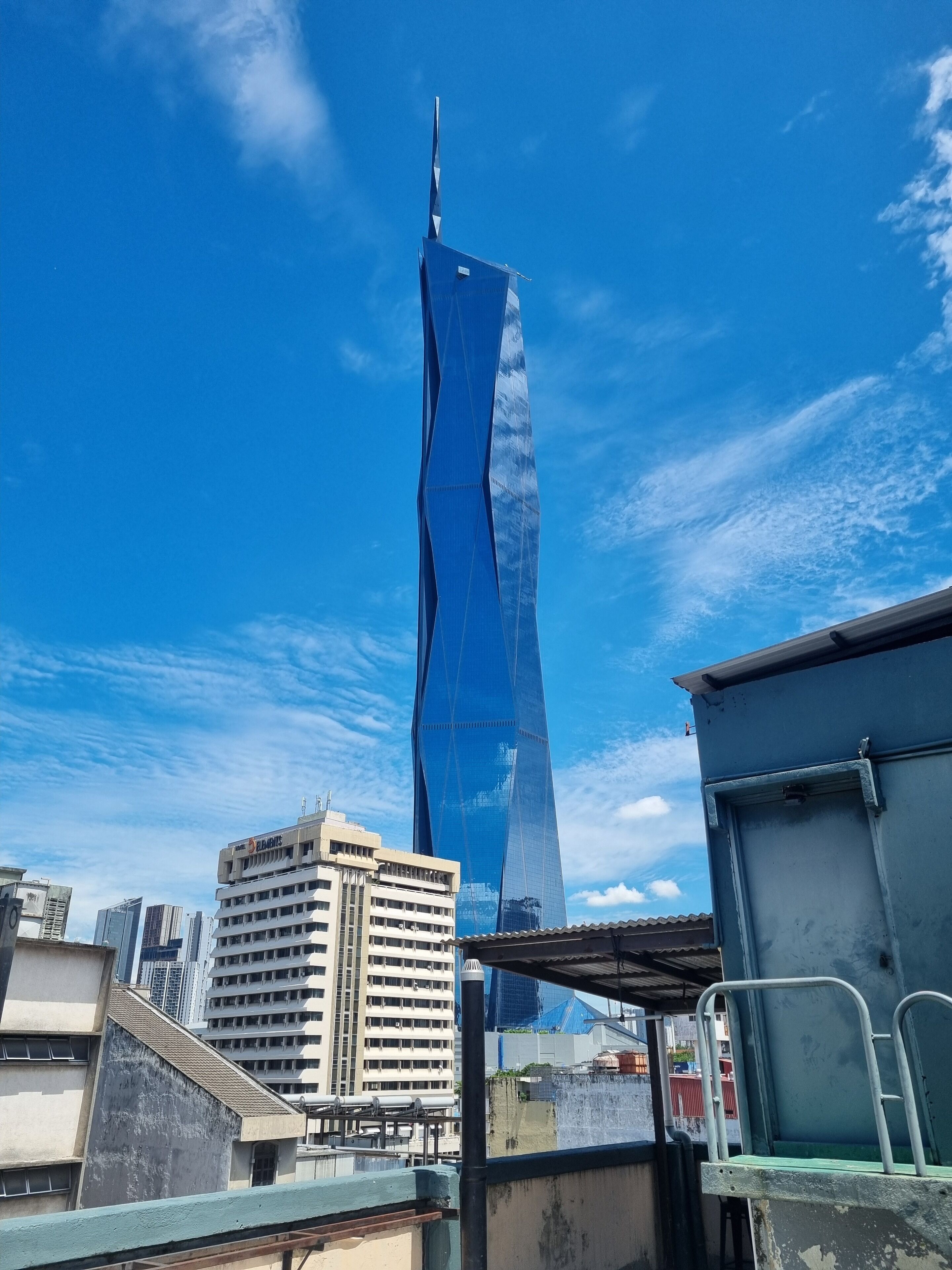 A modern skyscraper with a unique twisted design, surrounded by mid-rise buildings and a clear blue sky.
