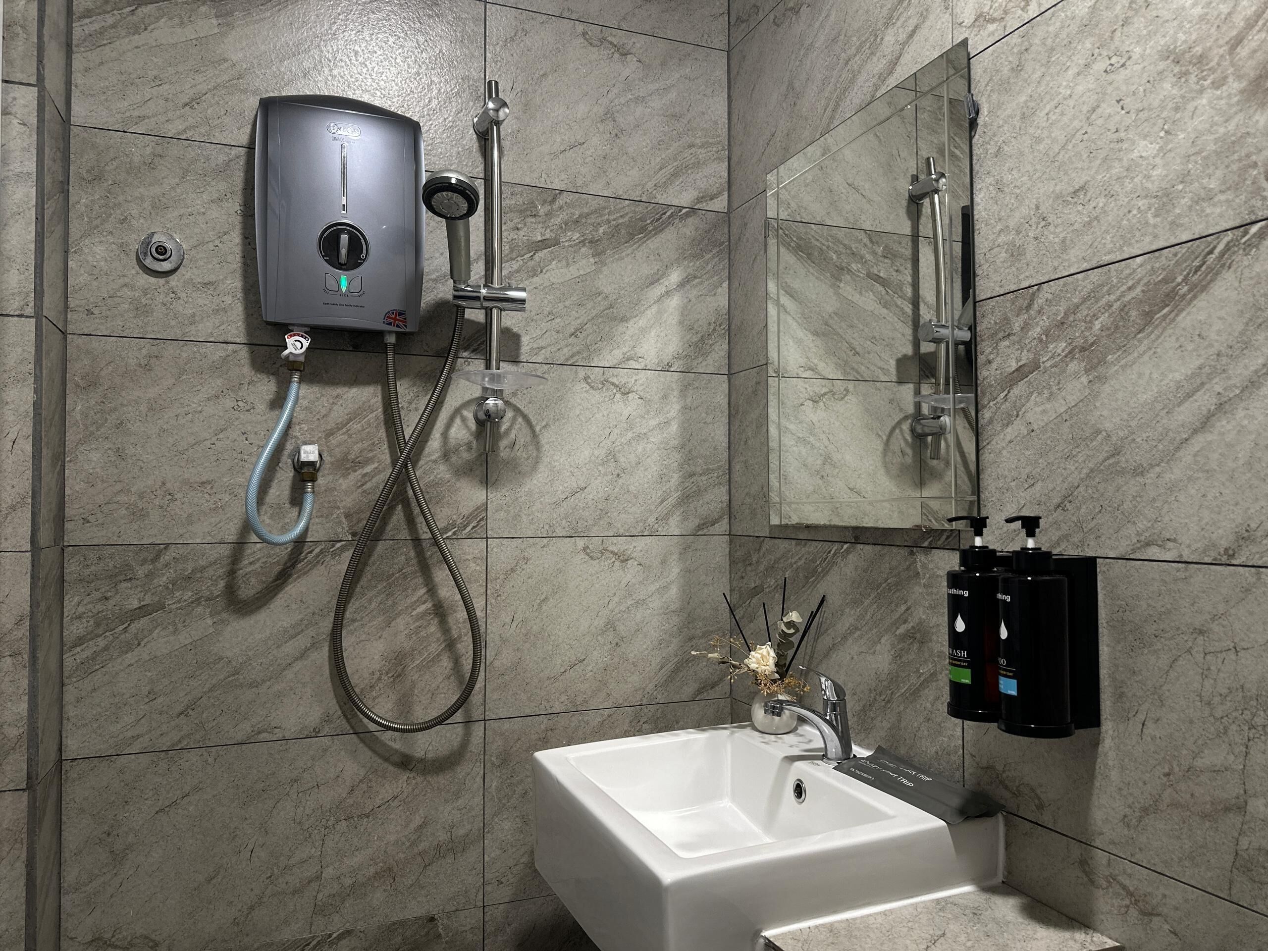A bathroom with a white sink, a handheld showerhead, a wall-mounted soap dispenser, and a mirror.