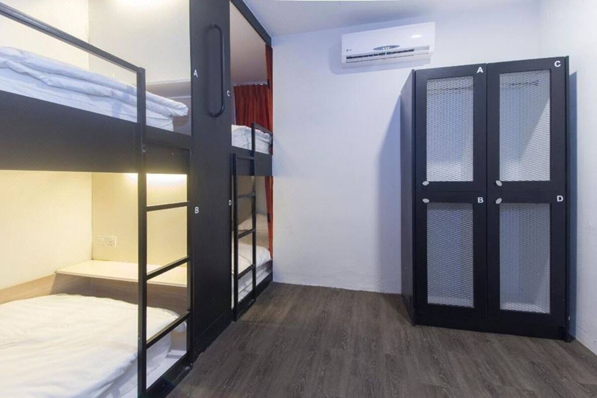 A compact room with bunk beds, a wardrobe with mesh doors, and a wall-mounted air conditioning unit.