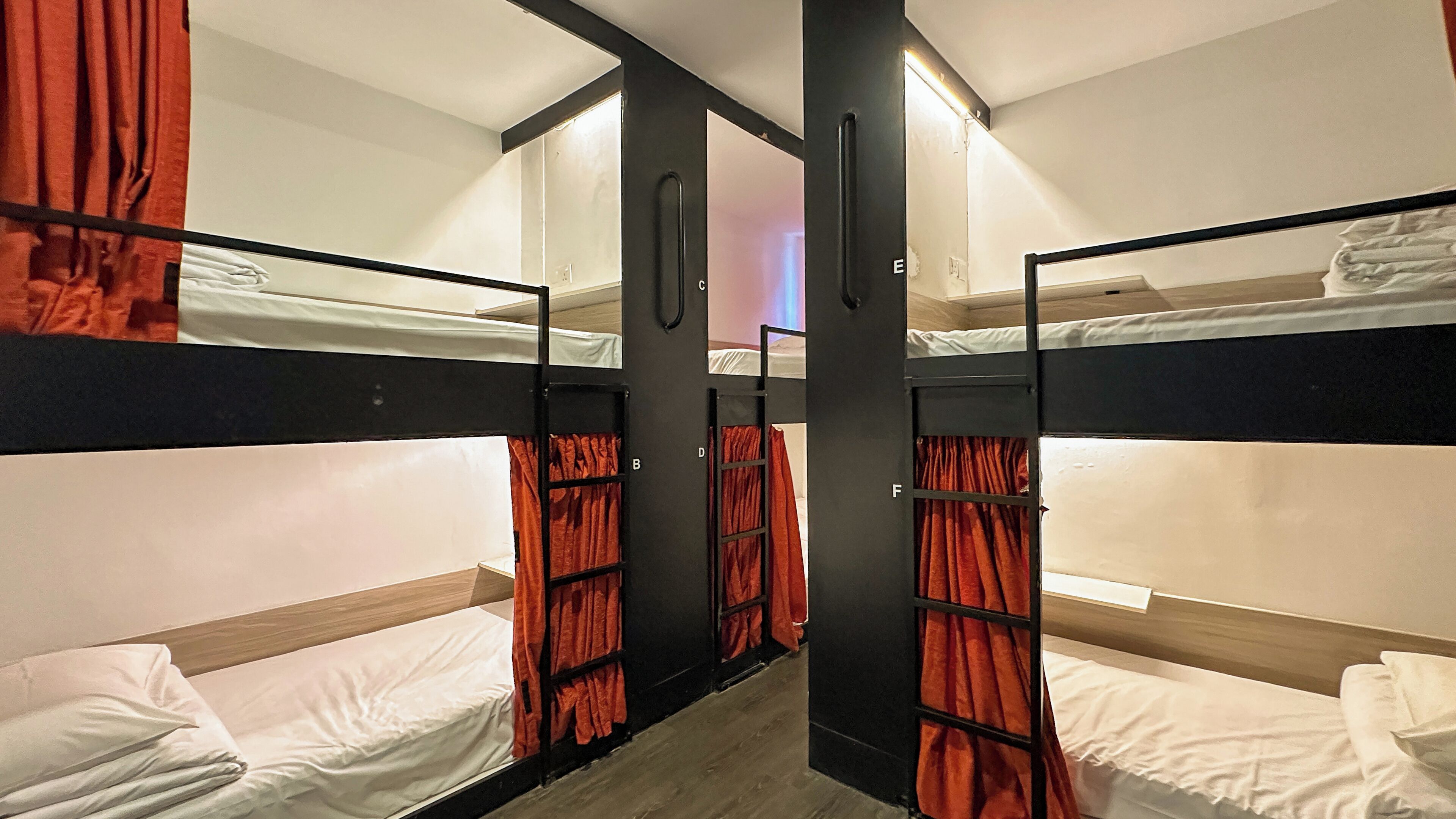 A dormitory room with bunk beds, red curtains, and a wooden floor.