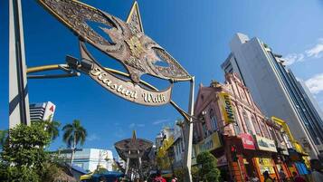 A large, ornate metal sign with the inscription "Kasturi Wall" in a bustling urban street with modern buildings and shops.