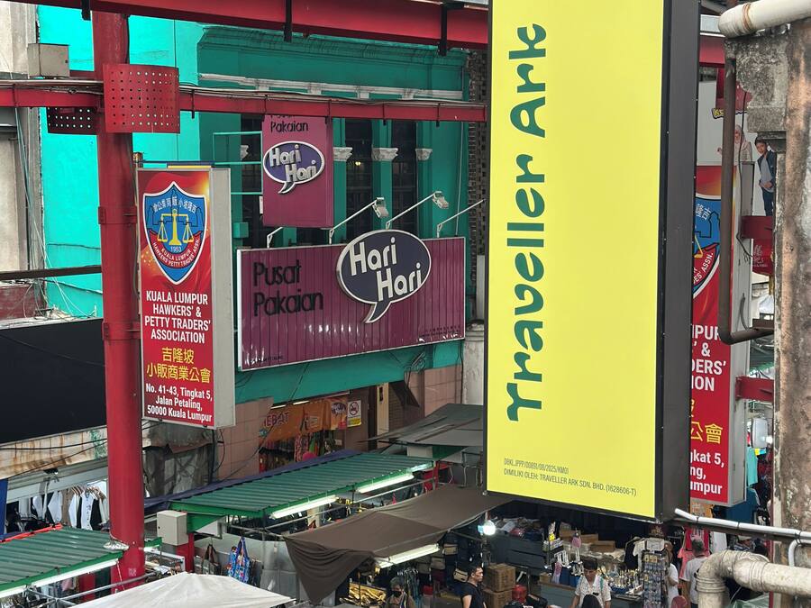 A market area with a prominent yellow sign for "Traveller Ark Hotel" and a "Hari Hari" shop.