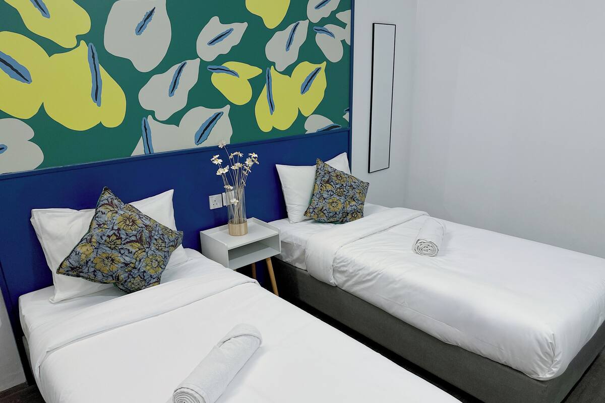 A hotel room with two single beds, white bedding, and a blue headboard.