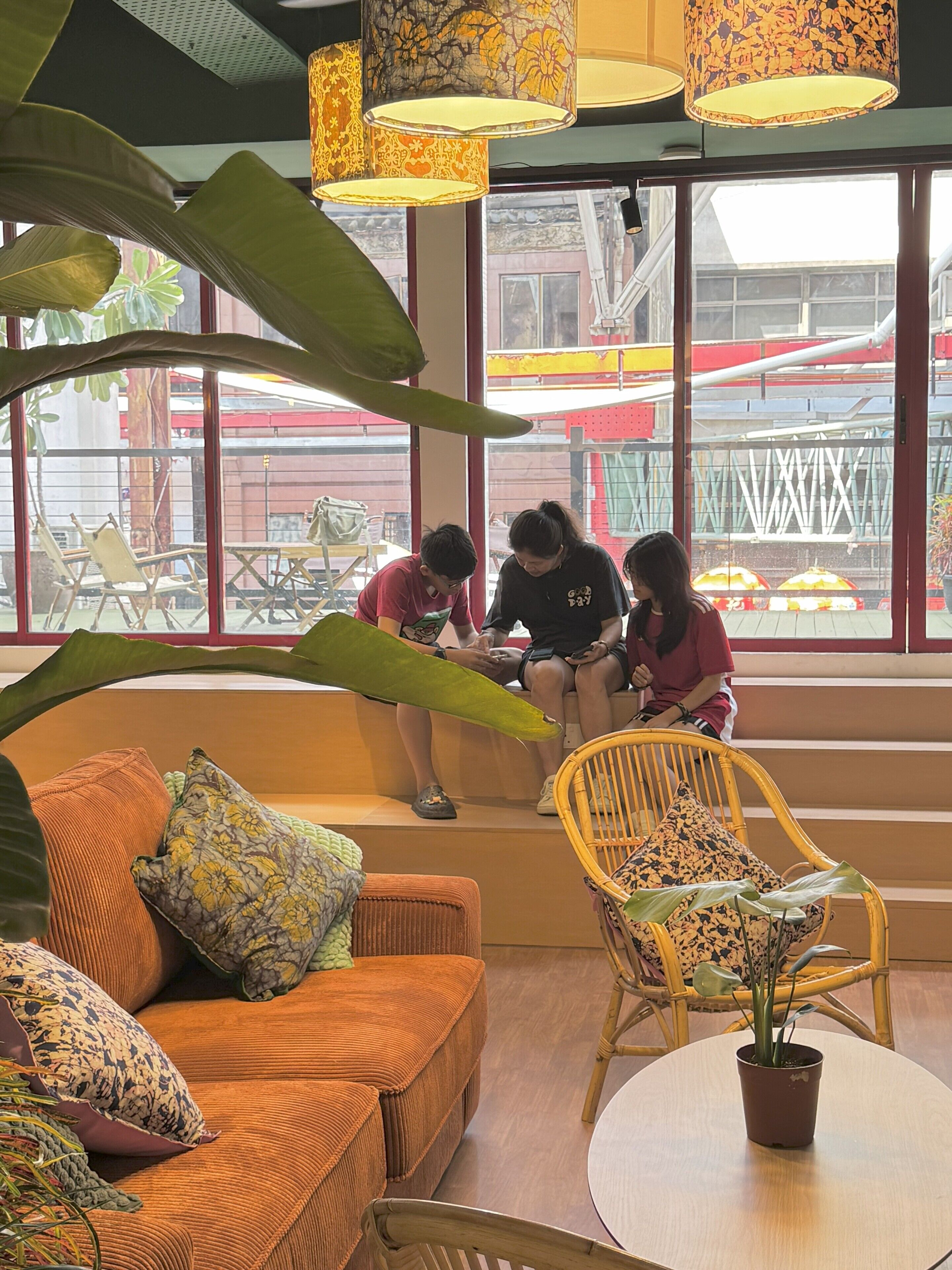 Un área de estar interior con sofá, sillas y una mesa. Se observan amplias ventanas con vista a un espacio exterior.