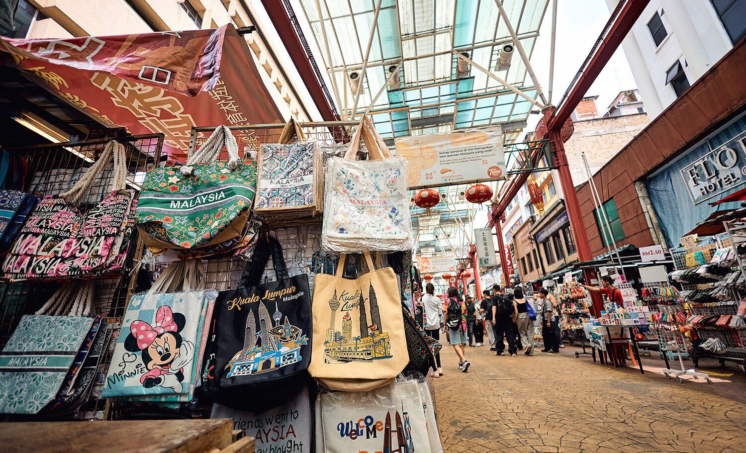 A bustling market street with various stalls selling bags and souvenirs.