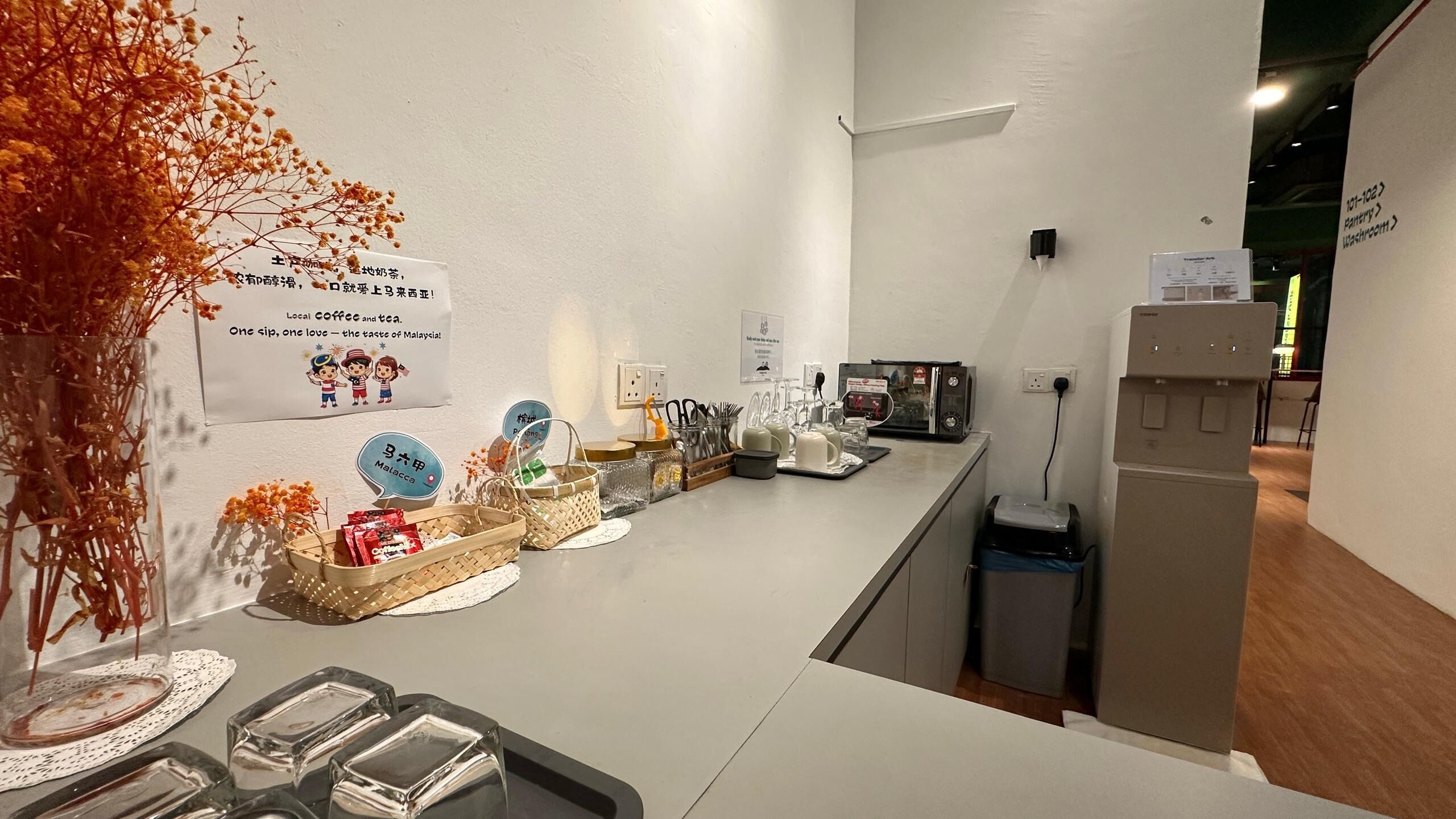 A counter with a coffee machine, tea kettle, and various condiments. There are signs indicating the location of the pantry and washroom.