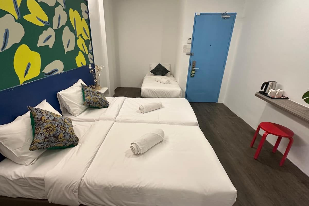 A hotel room with two beds, a red stool, a blue door, and a wall with a green and yellow abstract pattern.