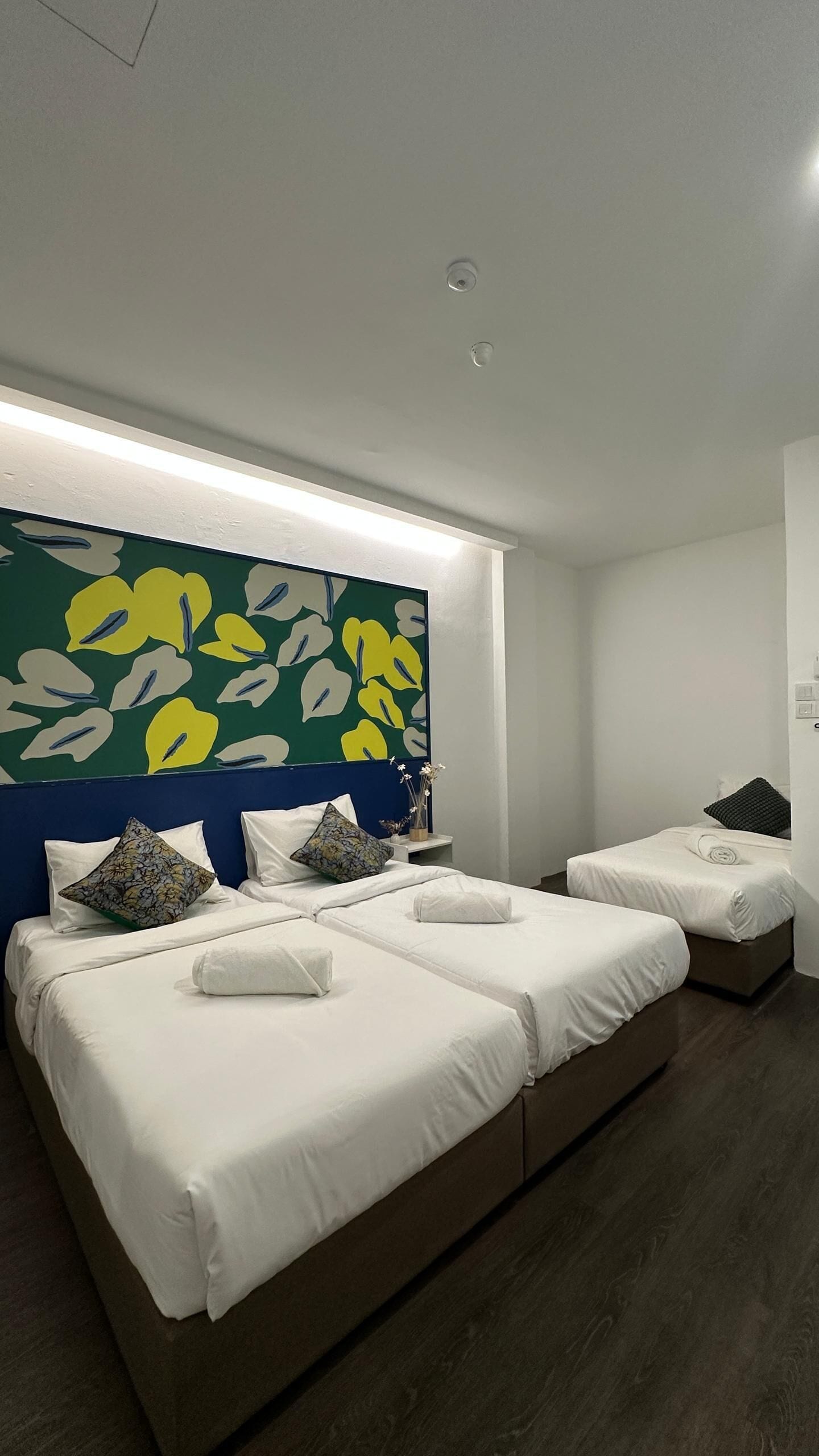 A modern hotel room with two beds, a large floral artwork on the wall, and a bedside table with a vase of flowers.