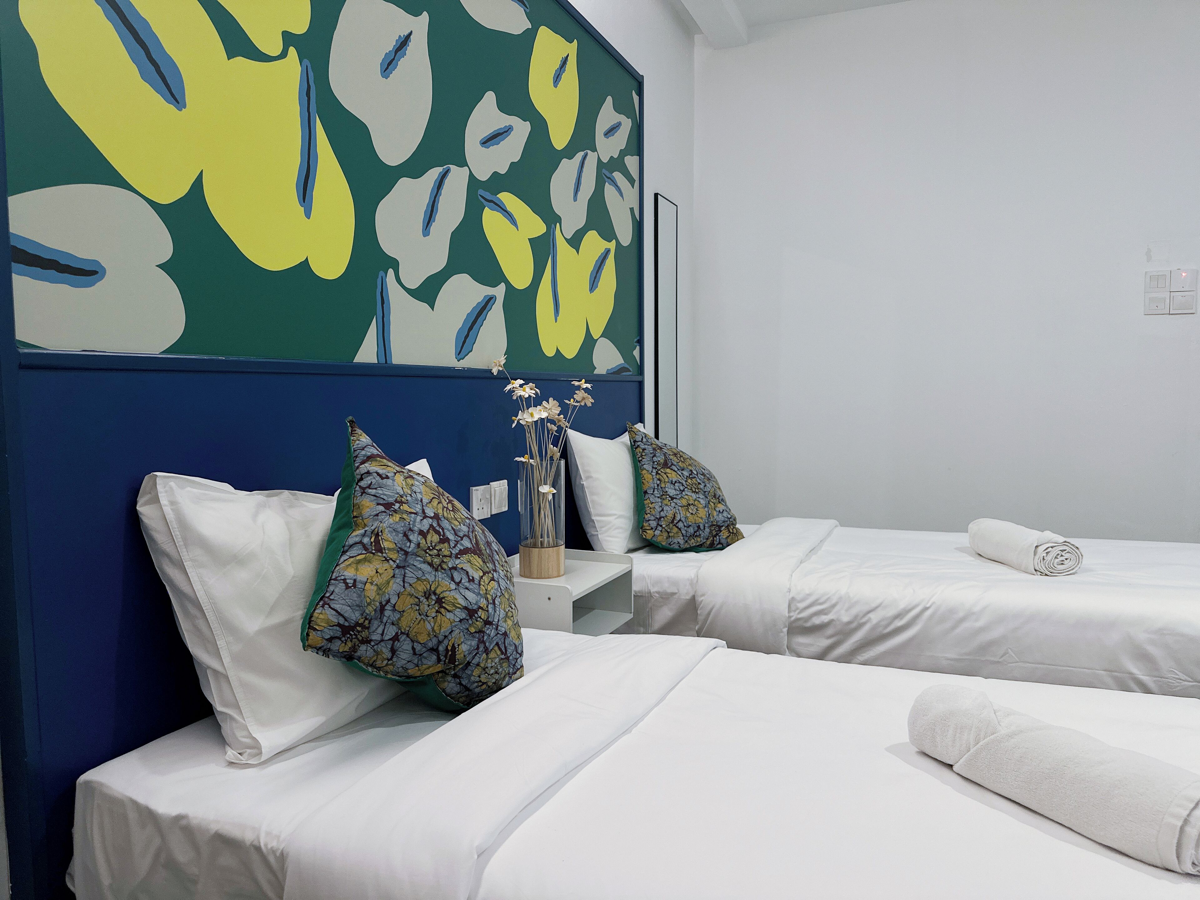 A hotel room with two beds, white bedding, a vase with flowers, and a colorful abstract painting on the wall.