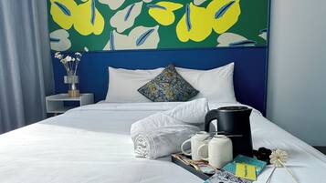 A hotel room with a bed, pillows, a nightstand, a vase with flowers, a tray with breakfast items, and a coffee maker.