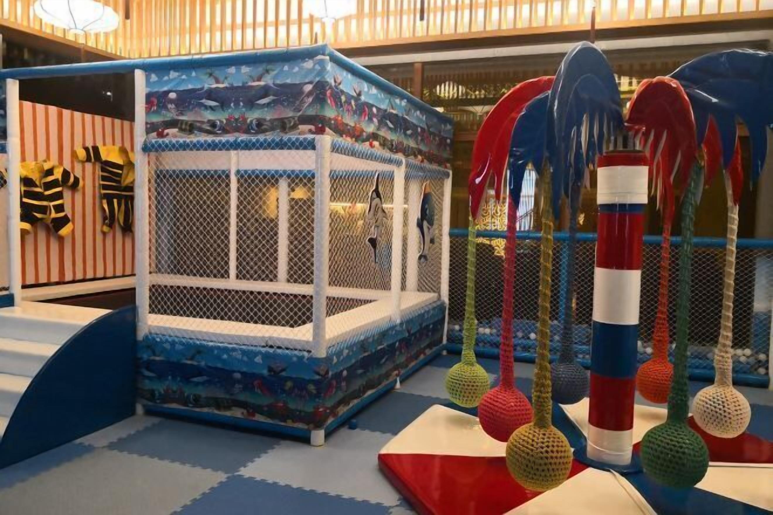 A play area with a blue and white playpen, colorful hanging toys, and striped fabric on the walls.
