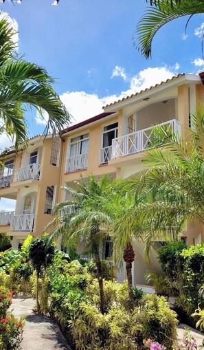Un immeuble à plusieurs étages doté de balcons, entouré d’une végétation luxuriante et surplombant un ciel dégagé.