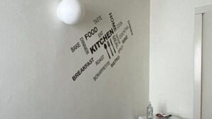 Eine Wand mit einer Wandsticker-Collage zum Thema Küche, einer Mikrowelle und einem kleinen Tisch mit einer Flasche.