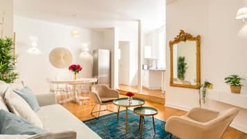 Una sala de estar moderna con un sofá, dos sillones, una mesa de centro y un comedor con una mesa y sillas. Se observa una cocina al fondo.