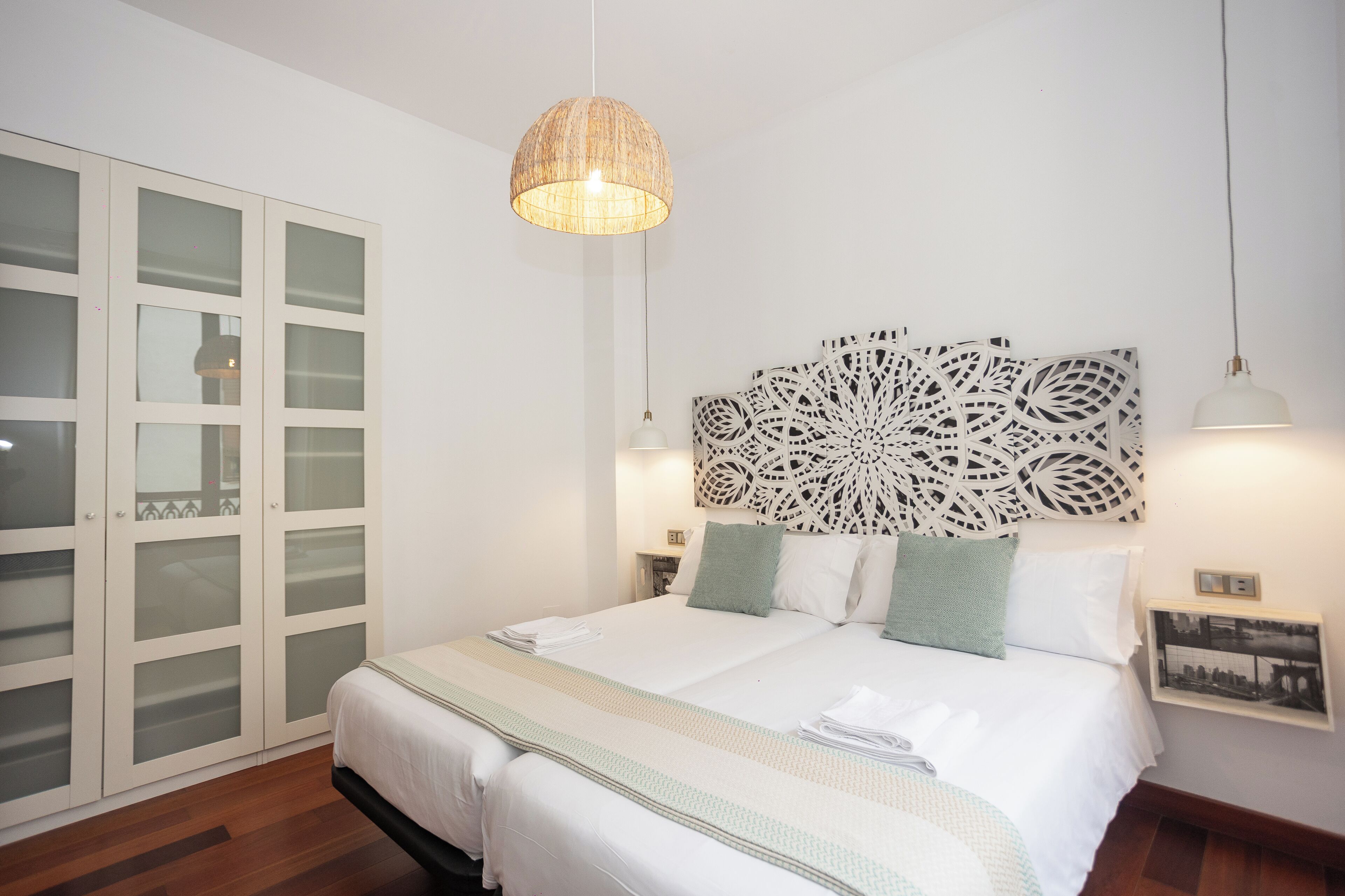 Un dormitorio con cama, cabecera decorativa, lámpara colgante, mesita de noche y armario.
