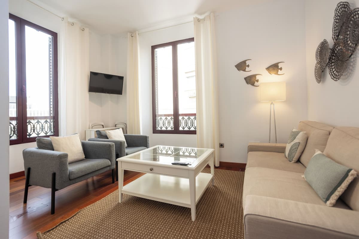Ein Wohnzimmer mit einer Couch, einem Sessel, einem Couchtisch, einem Fernseher und Wanddekorationen.