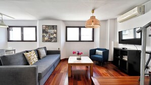 Ein modernes Wohnzimmer mit grauem Sofa, einem Holztisch, einem blauen Sessel, einem Fernseher und einer Klimaanlage.