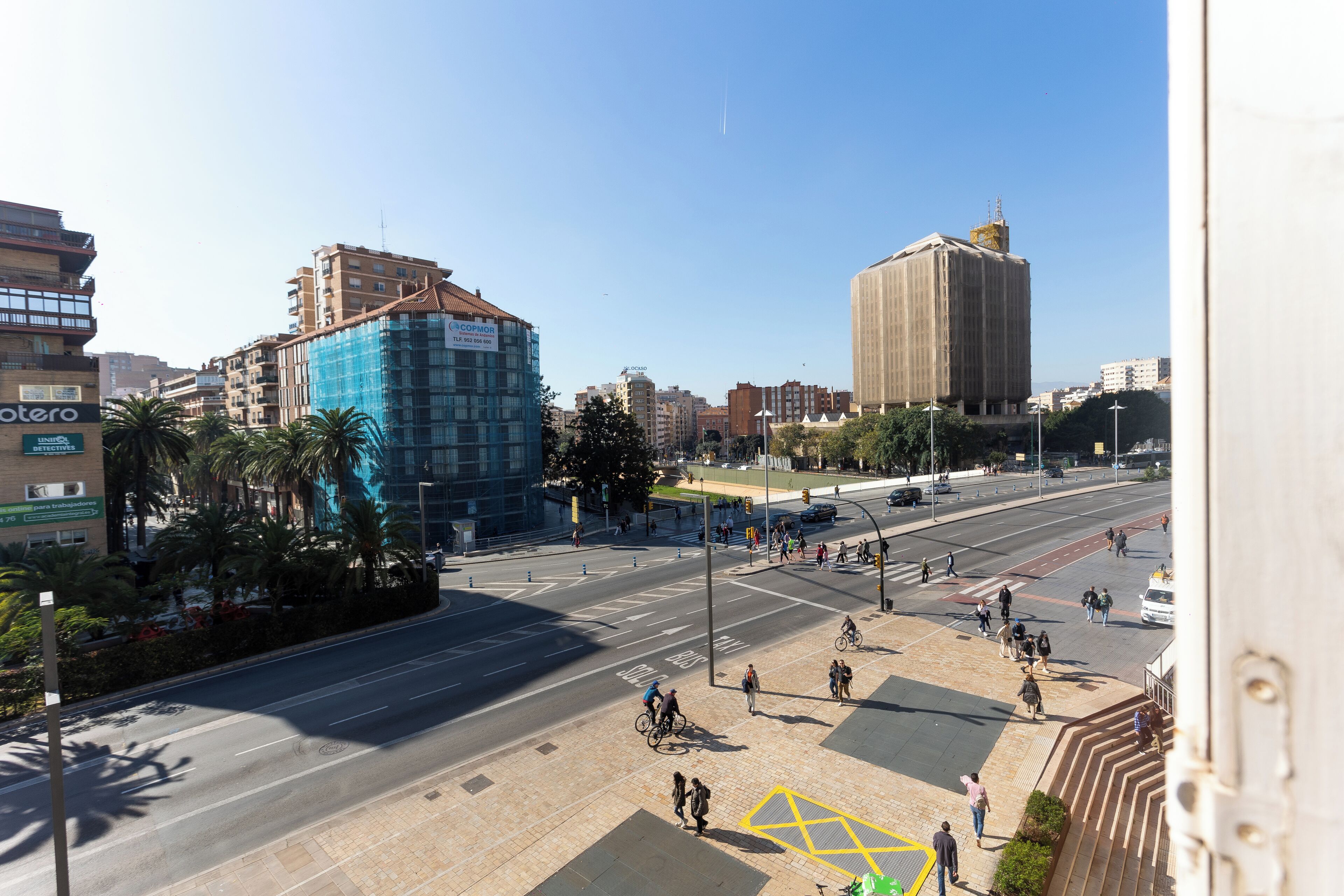 Une intersection animée en milieu urbain, avec des immeubles, des palmiers et un ciel dégagé.