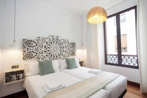 Un lit double avec du linge de lit blanc, une tête de lit décorative, des tables de chevet avec des lampes et une grande fenêtre offrant une belle vue.