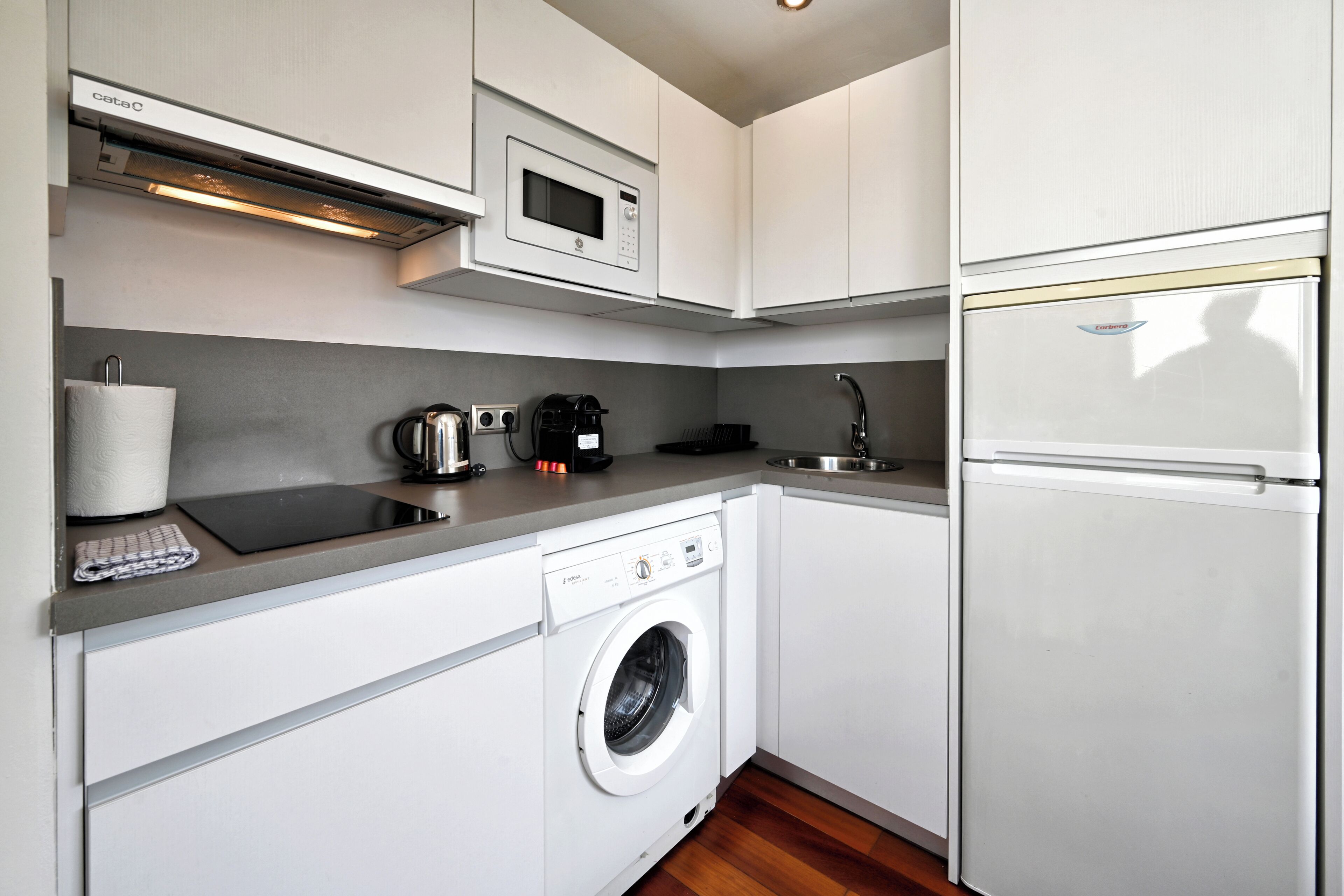 A compact kitchen with a built-in washing machine, a microwave, and a refrigerator.