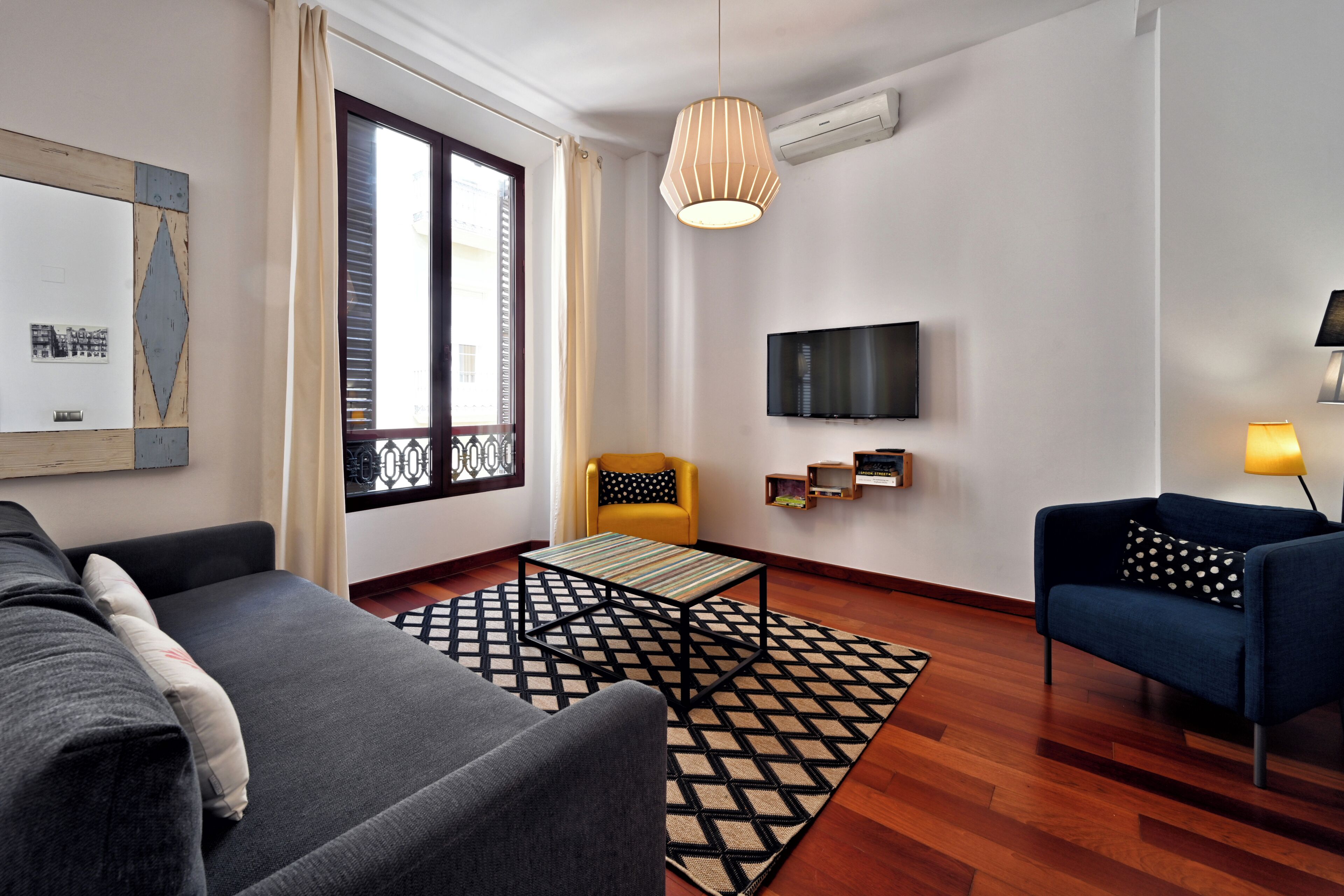A modern living room with a sofa, armchair, and a TV mounted on the wall.