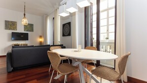 Ein modernes Wohnzimmer mit einem runden Esstisch, Korbstühlen, einem grauen Sofa, einem Flachbildfernseher und Kunstwerken an den Wänden.