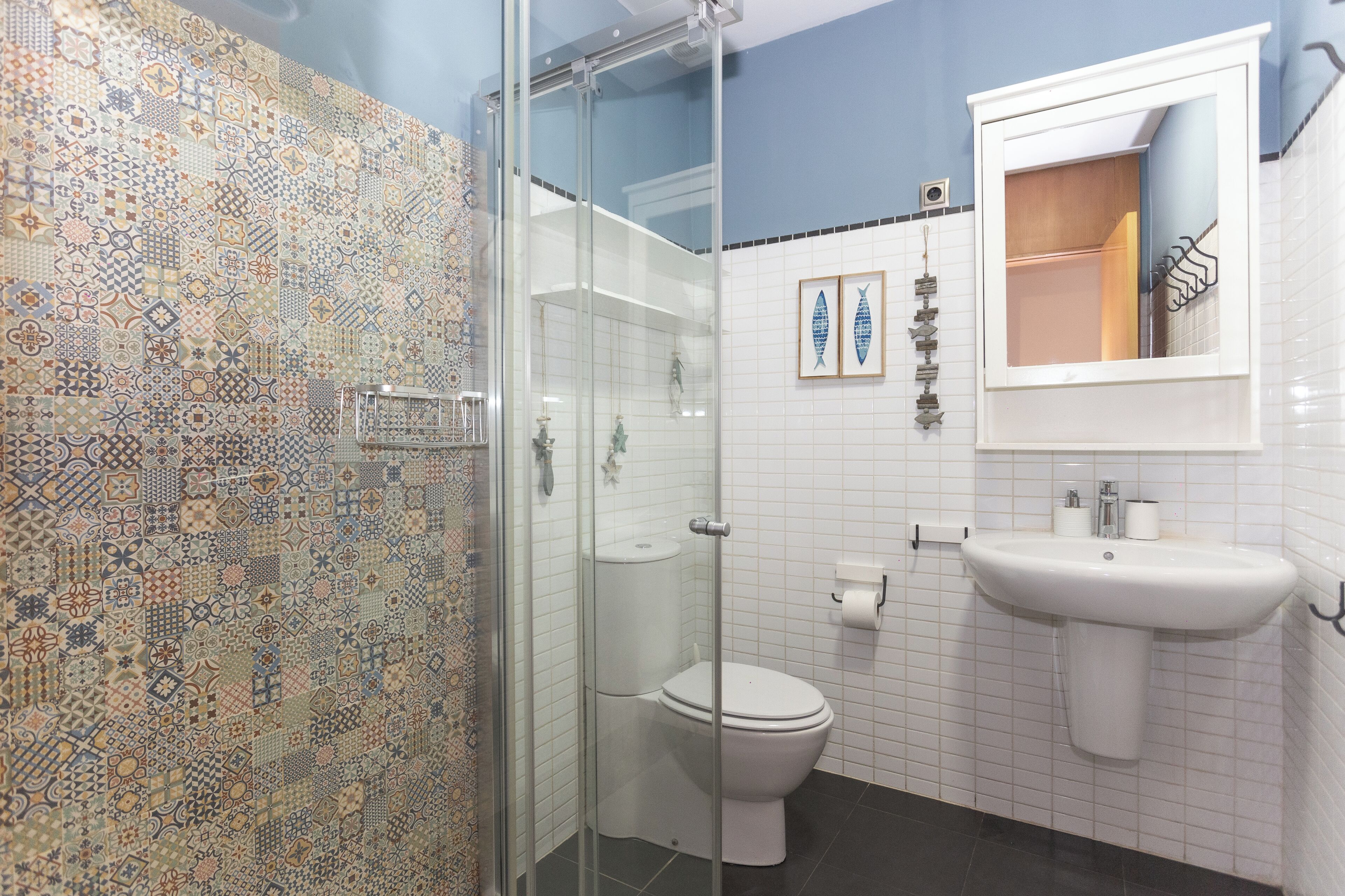 A bathroom with a patterned tile wall, a glass shower enclosure, a white toilet, and a sink with a mirror above it.