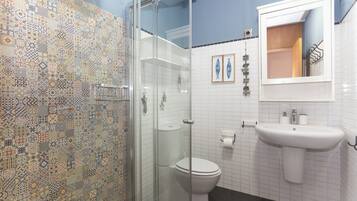 A bathroom with a patterned tile wall, a glass shower enclosure, a white toilet, and a sink with a mirror above it.