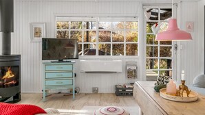 Un salon chaleureux avec une cheminée, un téléviseur et une grande fenêtre donnant sur les arbres.